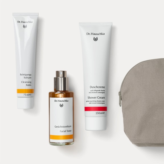 Duschcreme 150 ml, Gesichtstonikum Spray und Reinigungsbalsam 75 ml von Dr. Hauschka Naturkosmetik neben grauem Kulturbeutel