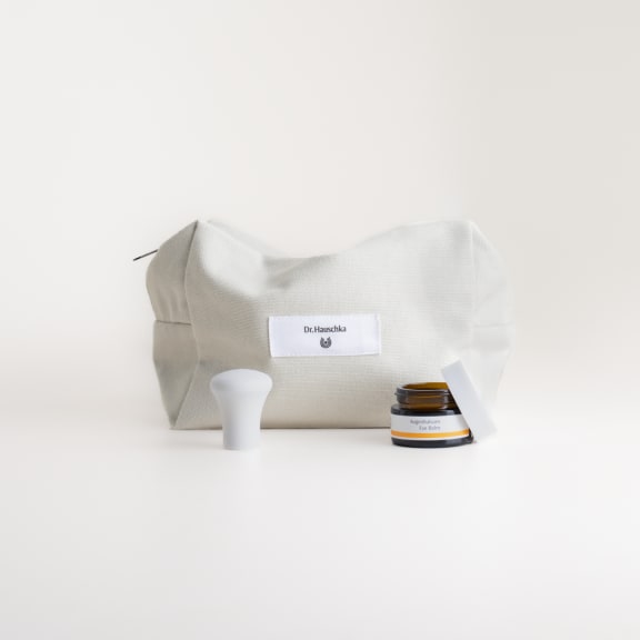 Augenbalsam von Dr. Hauschka Naturkosmetik neben beiger Kulturtasche