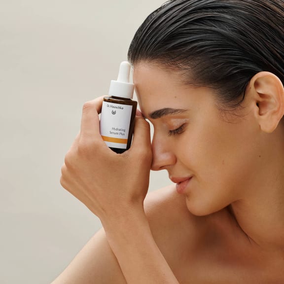 Hydrating Serum Plus von Dr. Hauschka Naturkosmetik, Modell hält braune Glasflasche