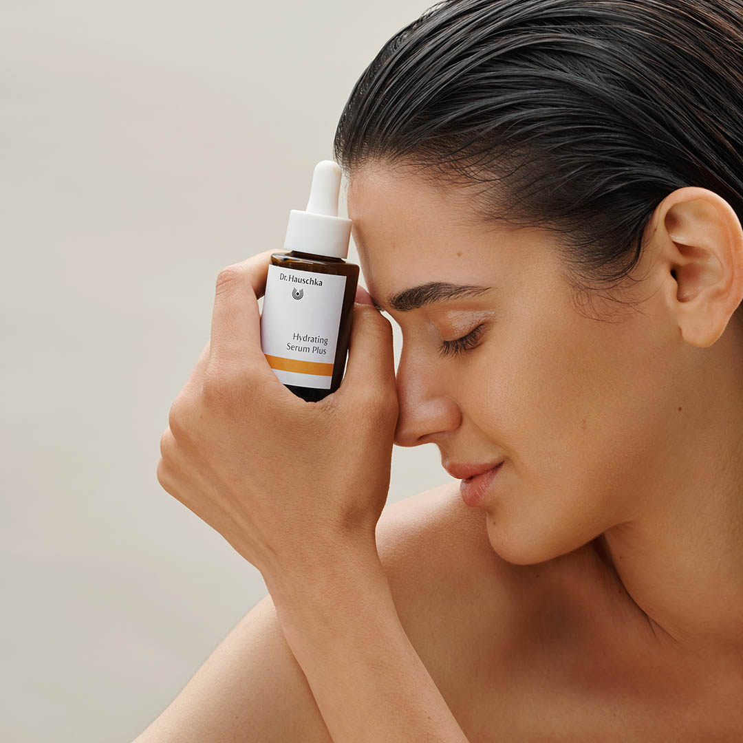 Hydrating Serum Plus von Dr. Hauschka Naturkosmetik, Modell hält braune Glasflasche