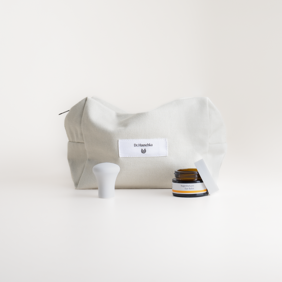 Augenbalsam von Dr. Hauschka Naturkosmetik neben beiger Kulturtasche
